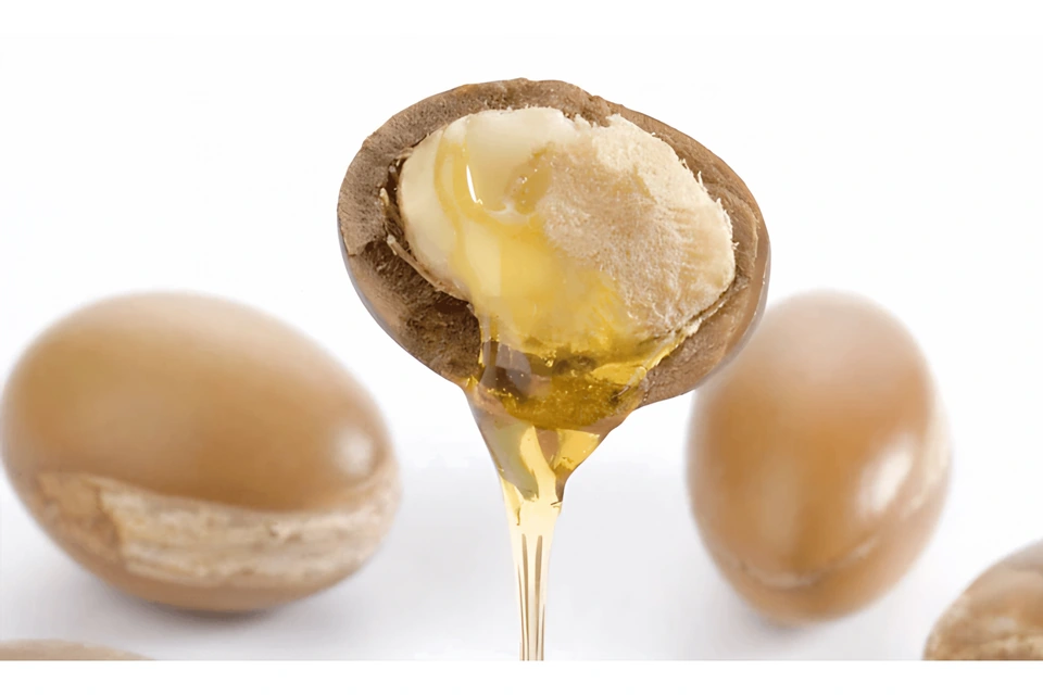 Aceite dorado goteando de una nuez de argán abierta, con nueces enteras detrás