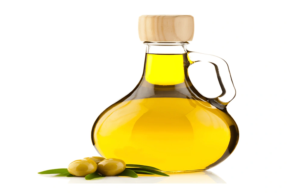 Aceitera de vidrio con aceite de oliva dorado, aceitunas verdes y hojas sobre fondo blanco